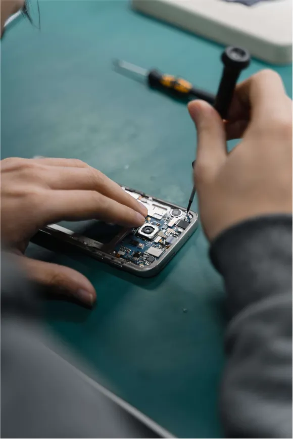 An image of a man fixing a phone on green surfac, seems to be unscrewing a screw at the back of the phone.